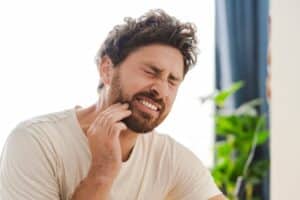 Portrait of young man holding his cheek in discomfort, showing signs of tooth pain potentially caused by infection or decay requiring root canal treatment